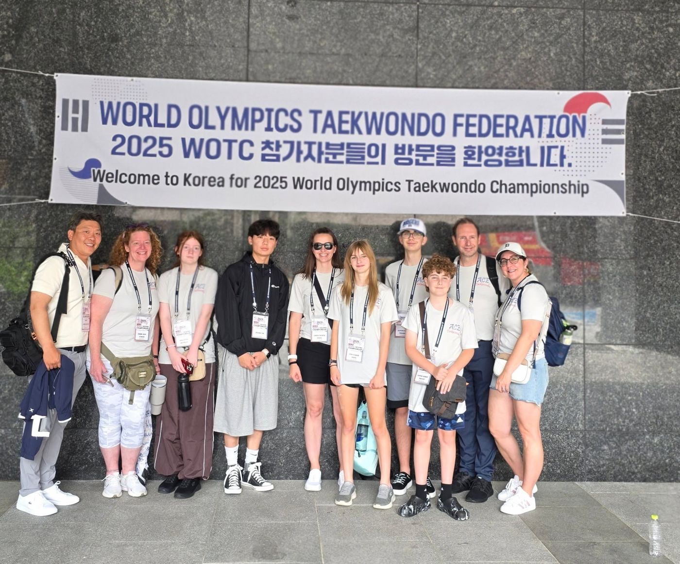 ACE students and families in Korea under a banner welcoming them to the 2025 World Olympics Taekwondo Championship
